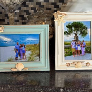 May include: Two framed photos with beach scenes. One frame is light blue, the other is off-white. Both are decorated with seashells and starfish. The photos inside show families on a beach.