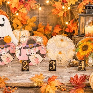May include: A Halloween-themed display featuring decorative plates with pumpkin and sunflower designs. A ghost figure with an orange hat and pumpkins is in the background. Pumpkins, fall leaves, and a lantern complete the festive scene.