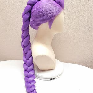 May include: A 32" dark purple wig styled with a long, thick, single braid that extends down the back. The hair is pulled back from the forehead with smooth sections, and the braid features a uniform, chunky weave ending in a loose, straight tail.