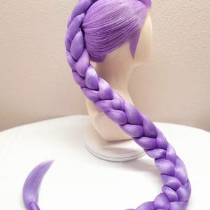 May include: A vibrant lavender wig styled with a thick, long, single braid that starts at the crown and extends down the back. The hair is smooth and synthetic, featuring a deep purple hue throughout, displayed on a neutral-toned mannequin head.