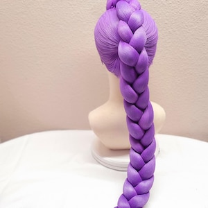 May include: A 32-inch dark purple synthetic hair extension styled in a thick, single braid on a mannequin head. The hair is smooth and vibrant, featuring a long, braided ponytail that extends downward, ending in a loose, straight section of hair.
