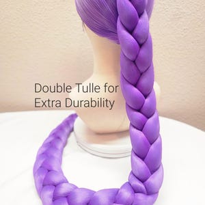 May include: A bright purple wig styled with a long, thick, single braid that extends downward. The wig is displayed on a mannequin head. Text on the image reads: Double Tulle for Extra Durability. The hair has a smooth, synthetic texture.