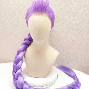 May include: A 50-inch light purple wig styled with a high bun and a long, thick braid that drapes forward. The wig is displayed on a mannequin head and features the text 50" Light Purple w/ Tulle at the top of the frame.
