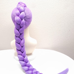 May include: A 32-inch light purple wig styled in a single thick, long braid that extends from the crown of a mannequin head. The hair is a solid lavender shade, and the braid is secured at the bottom with a small section of hair.