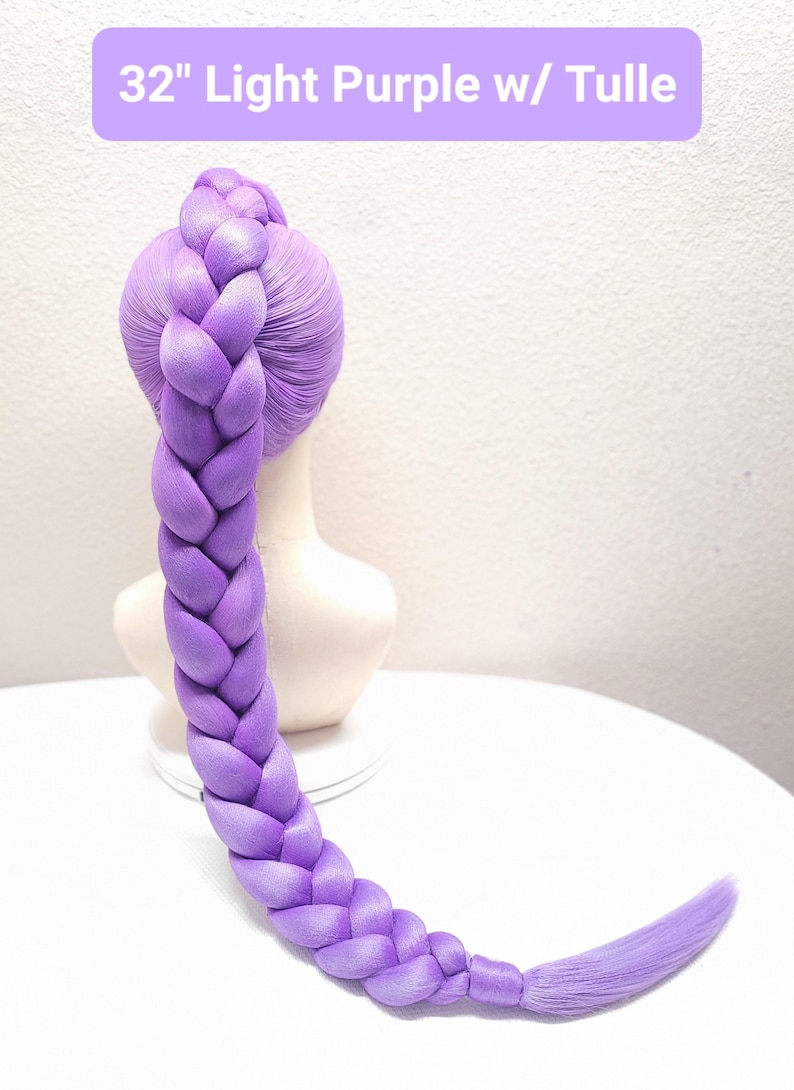 May include: A 32-inch light purple wig styled in a single thick, long braid that extends from the crown of a mannequin head. The hair is a solid lavender shade, and the braid is secured at the bottom with a small section of hair.