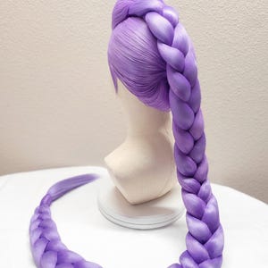 May include: A 50-inch light purple wig styled with a long, thick, single braid that extends from the crown of the head down to the base. The wig features smooth, straight hair fibers at the top and a large, uniform plait. Text reads 50" Light Purple w/ Tulle.