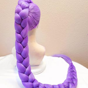 May include: A 50-inch dark purple synthetic hair extension styled in a thick, long braid. The hair is attached to a mannequin head and features a smooth, pulled-back crown section. The text 50" Dark Purple w/ Tulle is visible at the top.