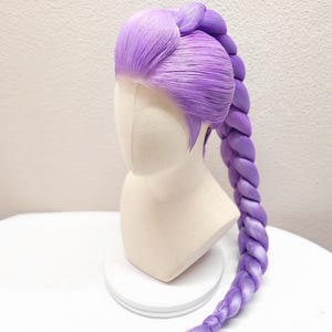 May include: A 32-inch light purple wig styled with a long, thick, single braid extending from the crown. The hair features a smooth, swept-back front section and a vibrant violet hue. The text 32" Light Purple w/ Tulle is visible at the top.