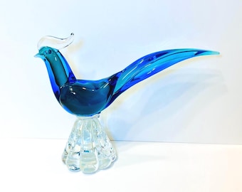 Könnte beinhalten: Eine blaue Glasvogelfigur mit einem klaren Glasfuß. Der Vogel hat einen langen Schwanz und einen gebogenen Kamm.