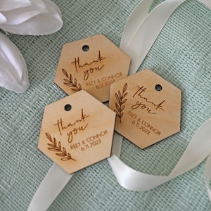 May include: Three hexagonal wooden thank you tags with a leafy branch design and the text "Thank you" in cursive. The tags also include the names "Riley & Connor" and the date "6.11.2023".