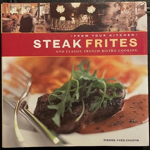 May include: A cookbook titled "Steak Frites: And Classic French Bistro Cooking" by Pierre-Yves Chupin, featuring a close-up image of a steak with a green garnish and a brown sauce on a white plate.