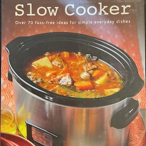 May include: A stainless steel slow cooker filled with a stew of meat, potatoes, and carrots. The image is from a cookbook titled "Slow Cooker" with the subtitle "Over 70 fuss-free ideas for simple everyday dishes."