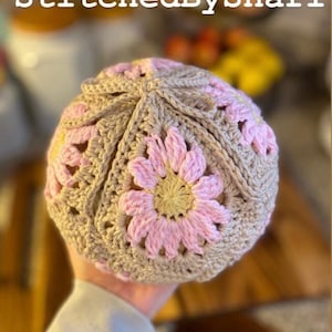 May include: A crocheted bread bag with pink and beige flowers. The bag is made of a soft, textured yarn and has a drawstring closure. The bag is shown with a loaf of bread inside.