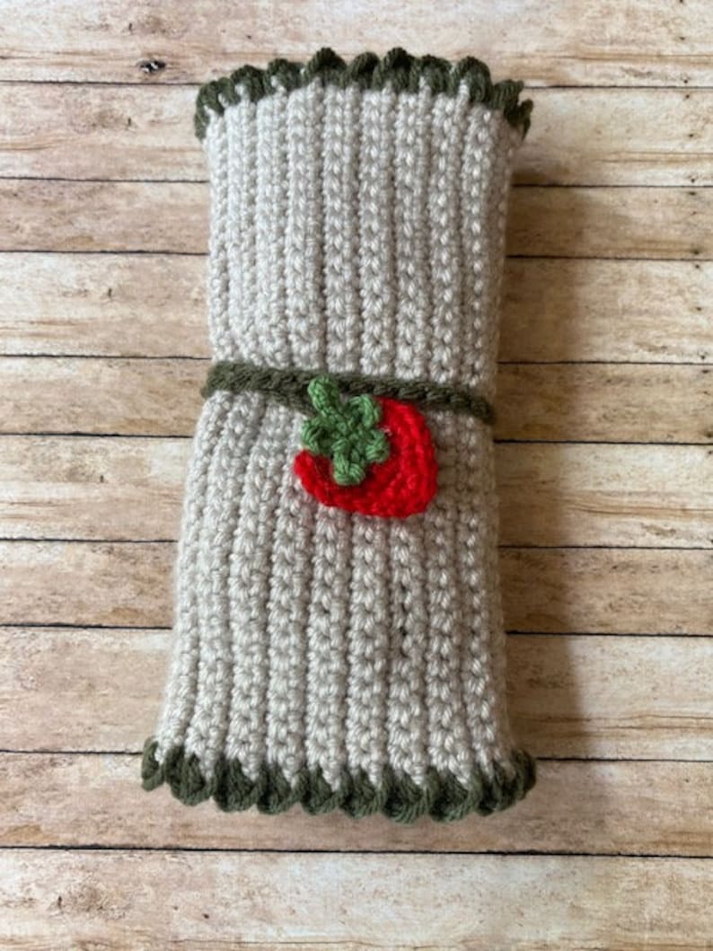 May include: A crocheted gray and green utensil holder with a red and green strawberry applique.