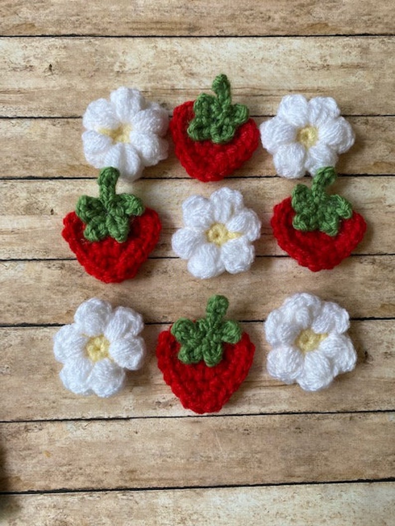 May include: Nine crocheted felt appliques, five white flowers and four red strawberries with green leaves.
