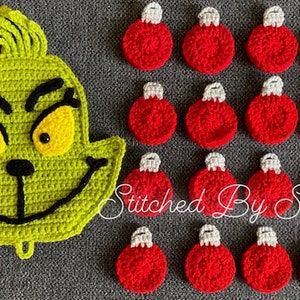 May include: Green crocheted Grinch face with yellow eyes and a black mouth.  There are 15 red crocheted ornaments with white tops.