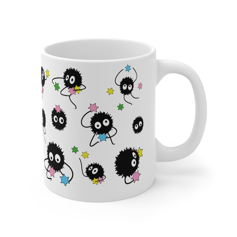May include: White ceramic mug with a black and white illustration of multiple fluffy black creatures with large eyes holding stars. The stars are in various colors including pink, blue, green, and yellow.