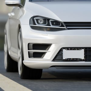 Puede incluir: Coche blanco con un marco de matr&iacute;cula negro con puntos de colores. El coche tiene una parrilla negra y faros negros.