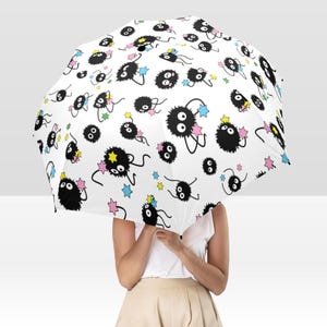May include: White umbrella with a repeating pattern of black, fluffy creatures and star accents in yellow, pink, and blue. The umbrella is open, held by a person. The design is whimsical and playful, perfect for a rainy day.