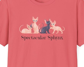 May include: Coral-coloured t-shirt with a graphic of four Sphynx cats in different poses. The text "Spectacular Sphynx" is printed beneath the cats. The shirt has short sleeves and a crew neck.
