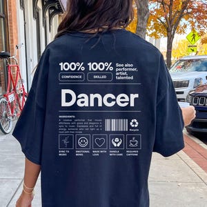 Può includere: Maglietta nera oversize con un design grafico bianco che dice "100% 100% Fiducia Abile" e "Ballerina". La grafica include anche icone per la musica, l'essere emotivo, l'amore, la manipolazione con cura e richiede caffeina.