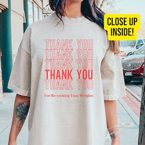 Peut inclure: Un t-shirt surdimensionn&eacute; beige clair avec le texte "THANK YOU" r&eacute;p&eacute;t&eacute; six fois en rouge. Le texte "For Re-racking Your Weights" est imprim&eacute; sous le texte r&eacute;p&eacute;t&eacute;.