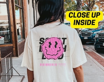 May include: A white t-shirt with a pink smiley face graphic. The graphic is made up of the words "Squat", "Bench", and "Dead" in a grid pattern. The text "#FOREVERSTRONG" is printed below the graphic.