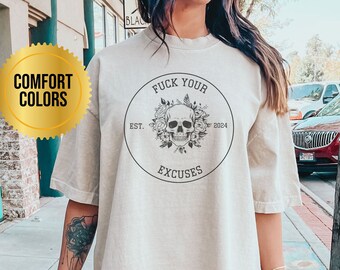 May include: An oversized beige t-shirt featuring a black circular graphic that reads "Fuck Your Excuses" with a skull and flowers within the circle. The text "Est. 2024" is positioned on the right side of the circle. The shirt has a relaxed fit and a distressed appearance.