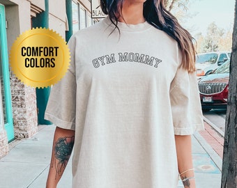 Può includere: Una maglietta oversize beige chiaro con il testo "GYM MOMMY" in nero. La maglietta è realizzata in un materiale morbido e confortevole.