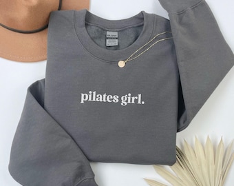 May include: A charcoal gray sweatshirt with the text "pilates girl." printed in white on the front.