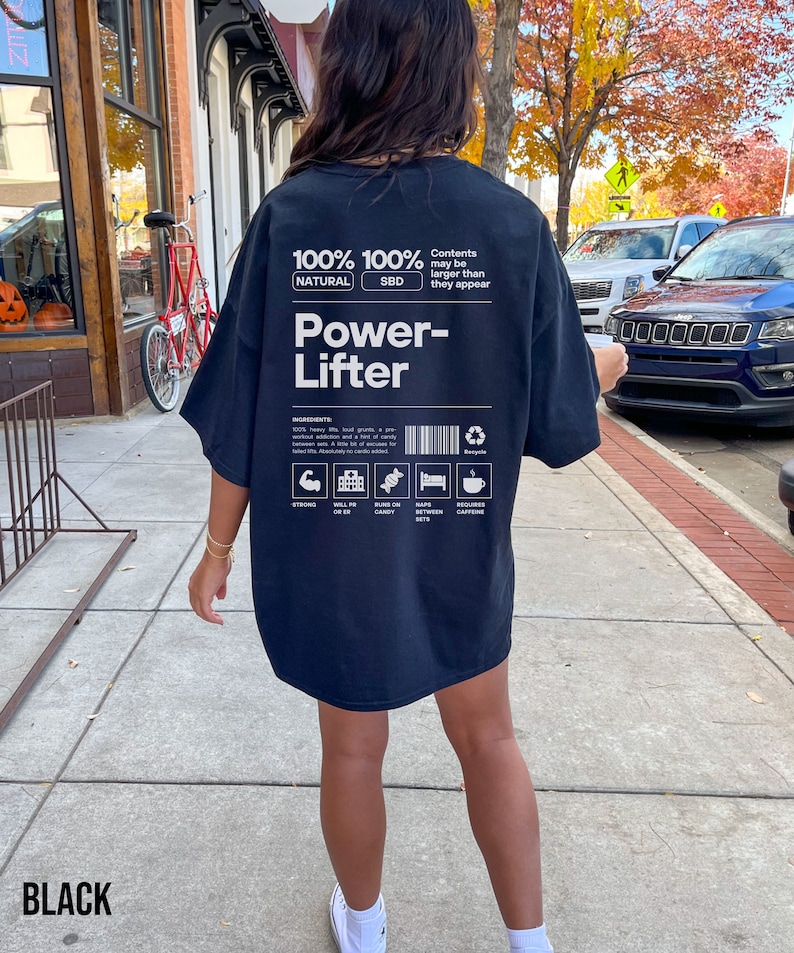 May include: Black oversized t-shirt with a white graphic design that says "100% Natural 100% SBD Power-Lifter" and includes a list of ingredients: "Strong, Will PR, Bund on Candy, Nap Between Sets, Requires Caffeine".