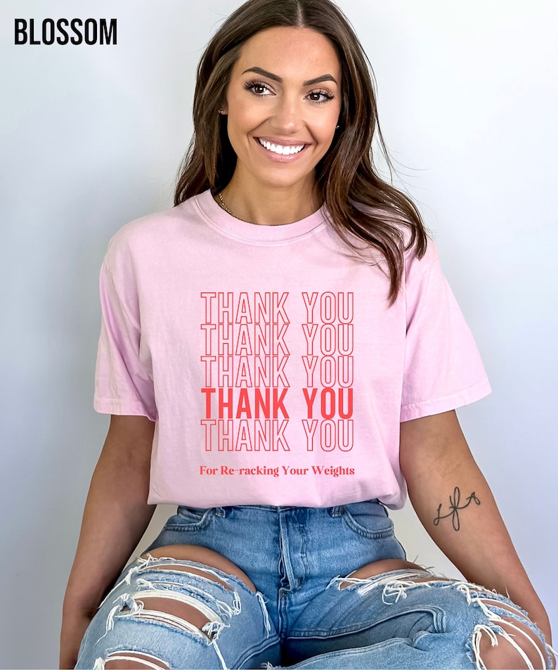 Peut inclure: T-shirt rose avec le texte "THANK YOU" r&eacute;p&eacute;t&eacute; cinq fois en rouge. Le texte "For Re-racking Your Weights" est imprim&eacute; sous le texte r&eacute;p&eacute;t&eacute;.