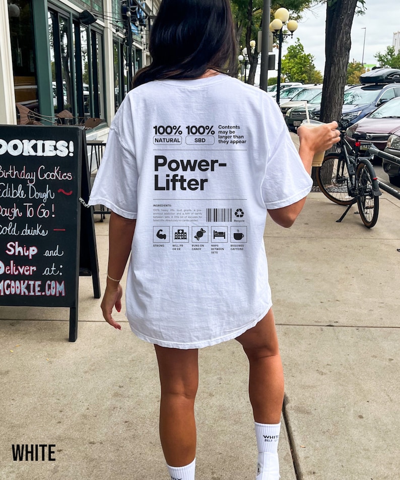 May include: White t-shirt with a black graphic on the back that says "100% 100% NATURAL SBD Power-Lifter". The graphic also includes icons for strong, will power, suns on candy, naps between sets, and requires caffeine.