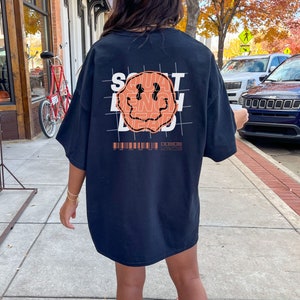 May include: Black oversized t-shirt with a graphic of a smiley face and the words "SQUAT BENCH DEAD" printed on the back. The graphic is in orange and white.