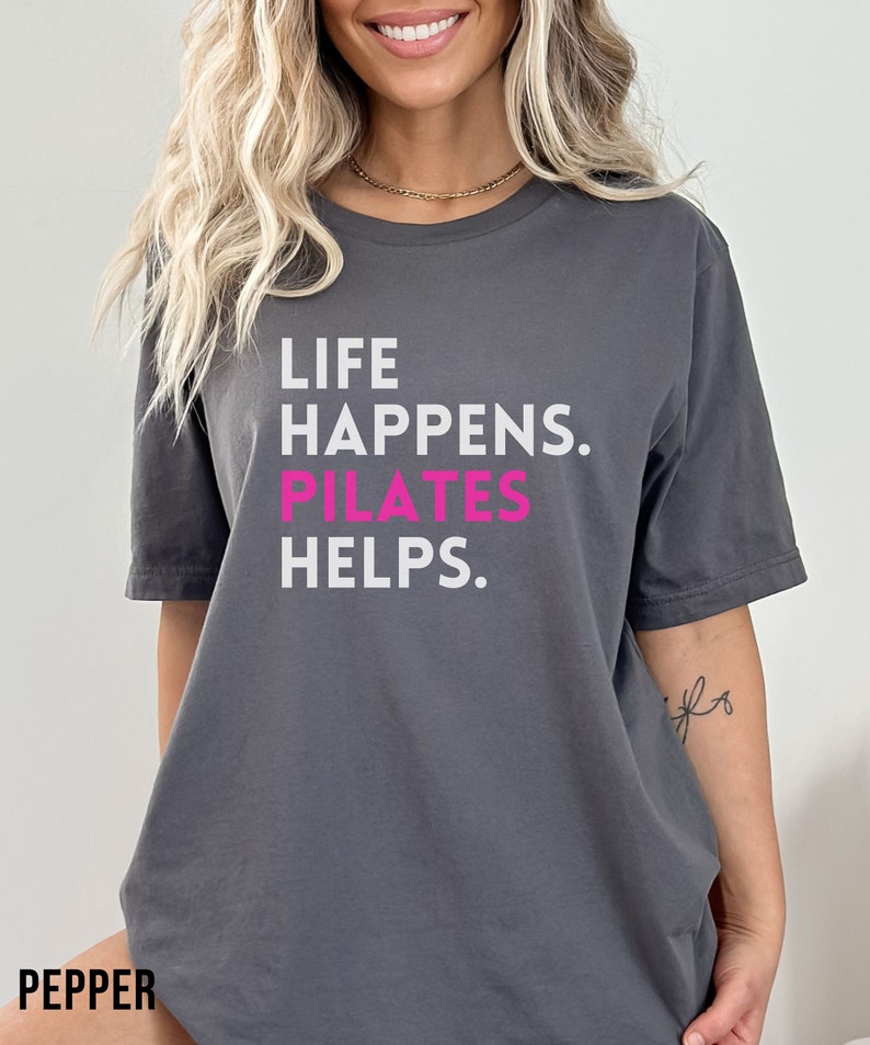 May include: Gray short-sleeved t-shirt with the text "LIFE HAPPENS. PILATES HELPS." in white and pink.