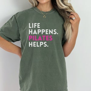 May include: A green t-shirt with the text "Life Happens. Pilates Helps." in white and pink lettering.