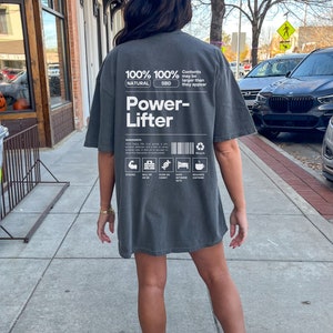 May include: A gray oversized t-shirt with a white graphic design that reads "100% Natural 100% SBD Power-Lifter" with a list of ingredients and icons. The text "Contents may be larger than they appear" is also included.