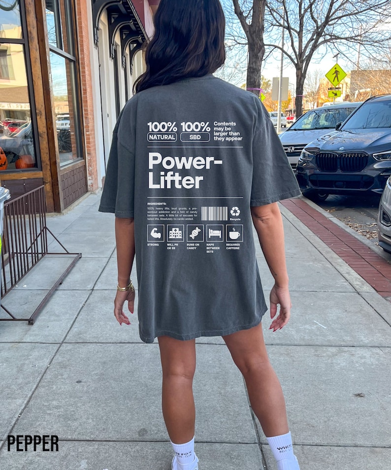 May include: A gray oversized t-shirt with a white graphic design that reads "100% Natural 100% SBD Power-Lifter" with a list of ingredients and icons. The text "Contents may be larger than they appear" is also included.