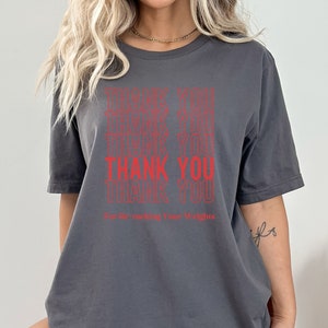 Peut inclure: T-shirt gris avec le texte "Thank You" r&eacute;p&eacute;t&eacute; plusieurs fois en rouge. Le texte "For Re-Racking Your Weights" est imprim&eacute; sous le texte r&eacute;p&eacute;t&eacute;.