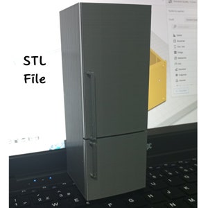 Puede incluir: Un modelo de refrigerador gris impreso en 3D con una manija de puerta. El modelo está sentado en un teclado de computadora portátil.