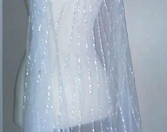 May include: A sheer white floor-length cape featuring vertical rows of shimmering silver sequins and beads. The lightweight fabric drapes from the shoulders, creating a translucent effect with a repeating linear pattern of reflective embellishments.
