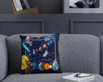 Op de afbeelding: Een blauw kussen met een kleurrijke illustratie van het zonnestelsel. Het kussen heeft cartoonfiguren, planeten en de zon. De tekst "Zonnestelsel" staat op het kussen gedrukt.