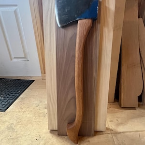 Puede incluir: Un hacha con mango de madera y cabeza pintada de azul, apoyada sobre una superficie de madera.