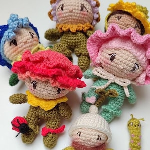 Peut inclure: Plusieurs poupées crochetées à la main, représentant des personnages-fleurs. Les poupées arborent des couleurs vives comme le bleu, le rose, le jaune et le vert, avec des visages détaillés et de petits membres. Une poupée a une coccinelle sur le pied.