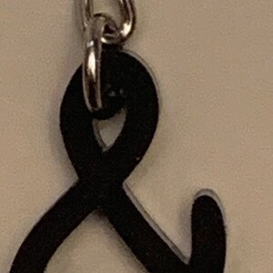 May include: A black ampersand charm attached to a silver chain.