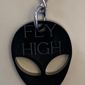 May include: Black alien-shaped keychain with the words "FLY HIGH" engraved on it.