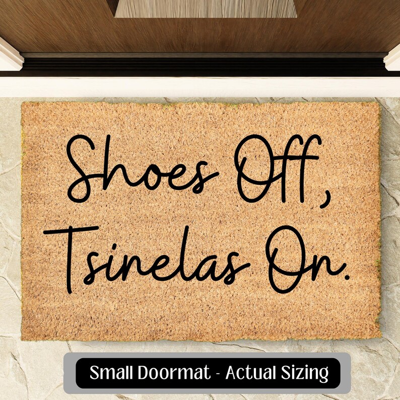 May include: A rectangular doormat with the text "Shoes Off, Tsinelas On" in black script. The mat is a light brown colour and has a textured surface. The words "Small Doormat - Actual Sizing" are in a black rectangle at the bottom.
