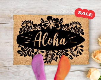 May include: A brown coir doormat with black floral designs and the word "Aloha" written on a surfboard.