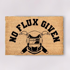 May include: A brown coir doormat with the text "No Flux Given" in black lettering. A welding helmet with crossed welding torches is centered below the text.