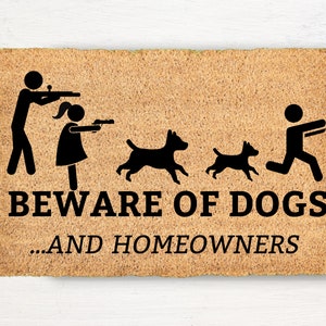 May include: A rectangular coir doormat with the text "BEWARE OF DOGS ...AND HOMEOWNERS" in black. The mat features stick figures of people with guns and dogs running away.